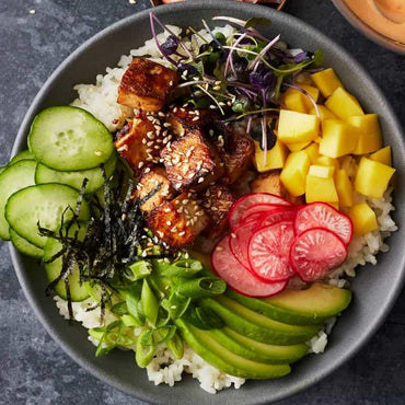 Colorful poke bowl with tofu, avocado, mango, cucumber, radish, seaweed, rice, and sesame seeds.