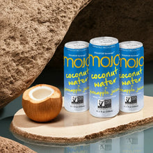 Cans of coconut water and pineapple juice with a halved coconut on a stone surface