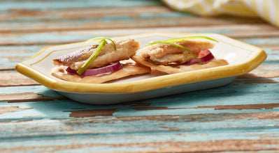 Crispy fish tacos with red onion and green garnish on ceramic plate, rustic wood background