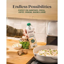 Hand holding Elmhurst Milked Cashews carton in kitchen, perfect for smoothies, cereal, coffee, cooking, baking