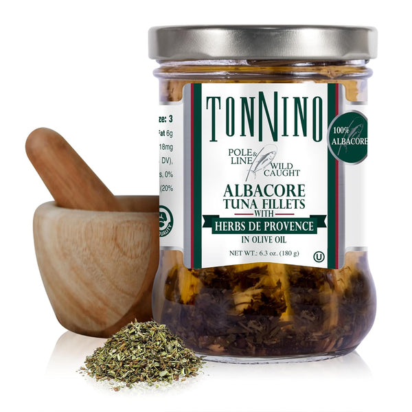 A glass jar of TonNino Albacore Tuna Fillets with Herbs de Provence in olive oil, shown with a wooden mortar and pestle and a small pile of the herbs on a white background.