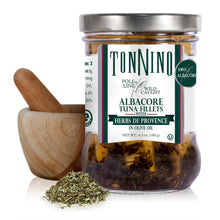 A glass jar of TonNino Albacore Tuna Fillets with Herbs de Provence in olive oil, shown with a wooden mortar and pestle and a small pile of the herbs on a white background.
