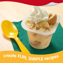 Banana pudding dessert cup topped with whipped cream and vanilla wafers with a yellow spoon.