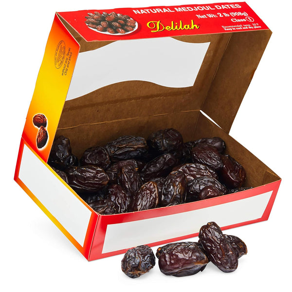 An open cardboard box of Delilah brand natural medjoul dates, with several dates spilled in front on a white background.