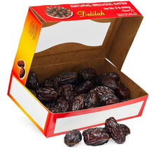 An open cardboard box of Delilah brand natural medjoul dates, with several dates spilled in front on a white background.