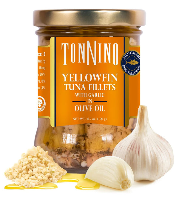 A jar of TonNino Yellowfin Tuna Fillets with Garlic in Olive Oil, shown on a white background with whole garlic bulbs, minced garlic, and a drizzle of yellow olive oil in front of the jar.