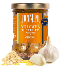 A jar of TonNino Yellowfin Tuna Fillets with Garlic in Olive Oil, shown on a white background with whole garlic bulbs, minced garlic, and a drizzle of yellow olive oil in front of the jar.