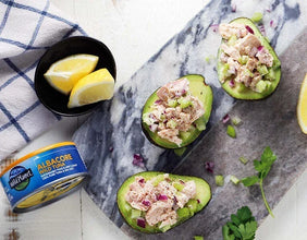 Avocado halves stuffed with tuna salad, chopped celery, and red onion, with lemon wedges and canned albacore tuna on a marble board