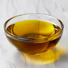 Clear glass bowl filled with golden cooking oil on a white marble surface
