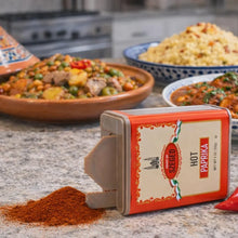 Hot Paprika spice tin with spilled red powder, kitchen counter, Hungarian dishes in background