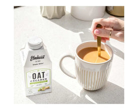 Elmhurst Oat Creamer Pistachio Crème next to coffee mug with spoon, plant-based dairy-free creamer