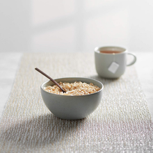 Bowl of puffed rice cereal with spoon and cup of tea on a textured placemat