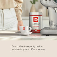 Ground coffee tin, espresso machine, and coffee cup on kitchen counter with person in background