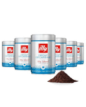 Six cans of illy decaf ground coffee with a pile of coffee grounds in front