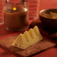 White chocolate bar with triangular segments on wooden board, warm candlelight background