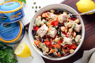 Bowl of tuna salad with chickpeas, artichokes, vegetables, and fresh lemon on table