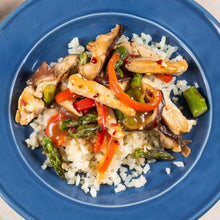 Stir fry chicken with bell peppers, mushrooms, and asparagus over rice on a blue plate