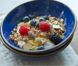 Healthy breakfast cereal with granola, yogurt, fresh berries, and sliced almonds in a blue bowl
