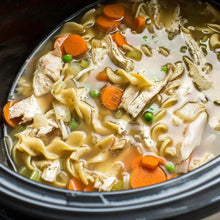 Homemade chicken noodle soup with carrots, peas, and celery in a slow cooker