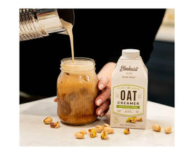 Elmhurst Oat Creamer Pistachio Crème being poured into iced coffee, plant-based dairy-free creamer with scattered pistachios