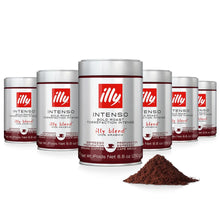 Multiple cans of illy Intenso bold roast ground coffee with a pile of coffee grounds in front
