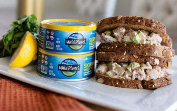 Wild Planet canned tuna next to tuna salad sandwich on whole grain bread with lemon slice