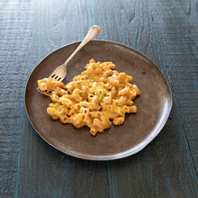 Creamy macaroni and cheese on a rustic brown plate with a fork on dark wooden table