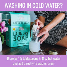 Person dissolving fragrance free laundry soap powder in jar of water, laundry soap box on table.