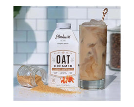 Elmhurst Oat Creamer Caramel Macchiato flavor next to iced coffee drink and spilled topping