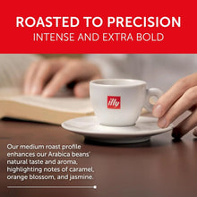 Hand holding espresso cup with illy logo, medium roast coffee, roasted to precision, close-up.