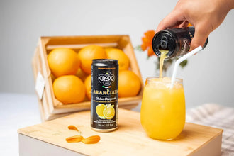Pouring Italian orangeade from Crodo can into glass with ice, fresh oranges in crate nearby
