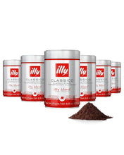 Six cans of illy Classico ground espresso coffee with a pile of coffee grounds in front
