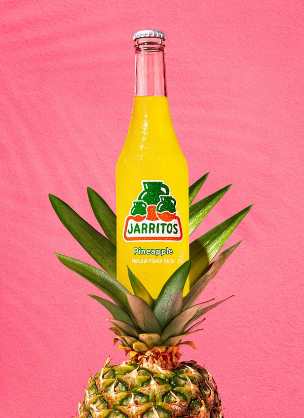 Jarritos Pineapple soda bottle on a pineapple with a pink background